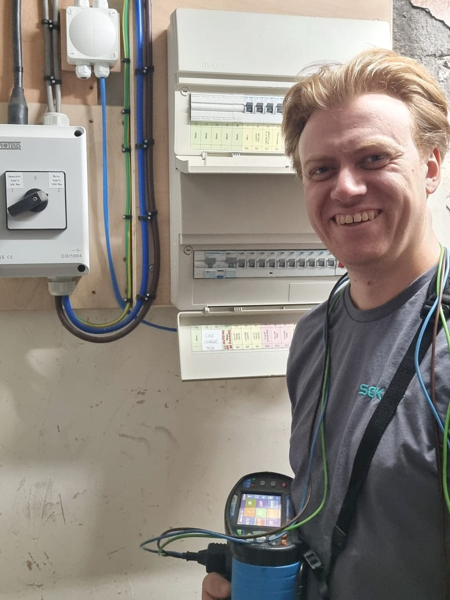 Dave, owner and electrician at SOKKIT, holding electrical test equipment beside a consumer unit